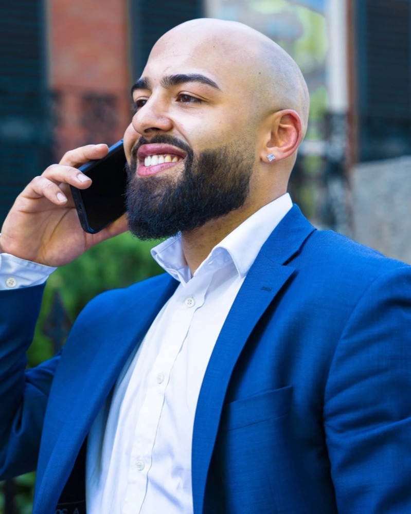 Xavier S. Cole in a blue blazer, smiling on a phone call outside a brick building